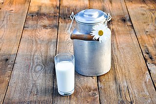 Ein Glas Milch steht vor einer Milchkanne. 