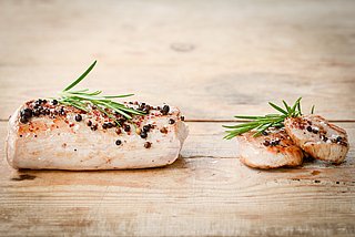 Mehrere Stücke gebratenes Schweinefleisch liegen garniert mit Gewürzen auf einem Holzbrett.