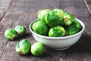 Mehrere Rosenkohlköpfchen liegen in einer Schüssel. Neben der Schüssel liegen weitere Rosenkohlköpfchen verteilt. 