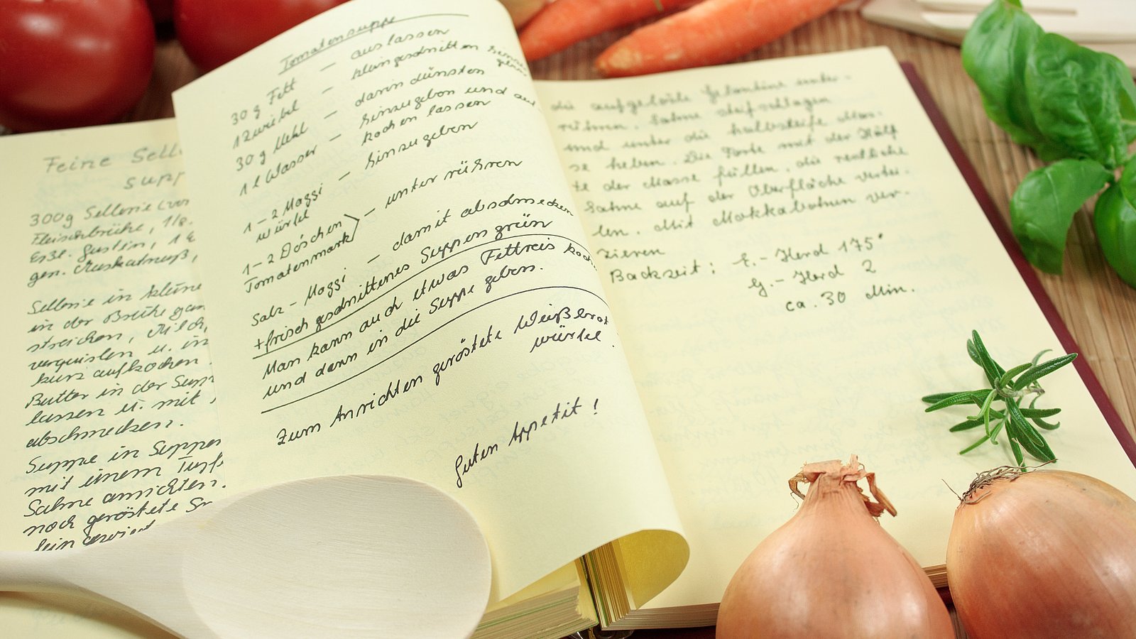 Handgeschriebenes Kochbuch liegt aufgeschlagen da, rundherum Gemüse und Kochutensilien