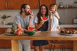 Ein kleines Kind isst mit seiner Mutter und seinem Vater Wassermelone in der Küche.